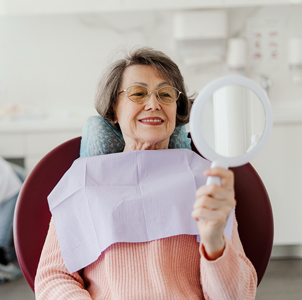 Female dental patient in pink sweater checking smile in handheld mirror