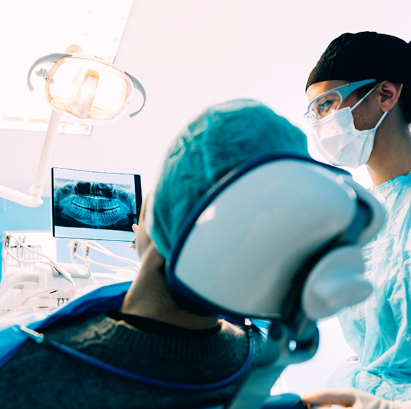 Dentist wearing mask showing X ray to patient in dental chair