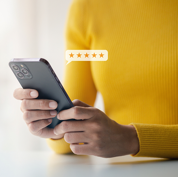 Woman in yellow shirt looking at 5 star review on phone