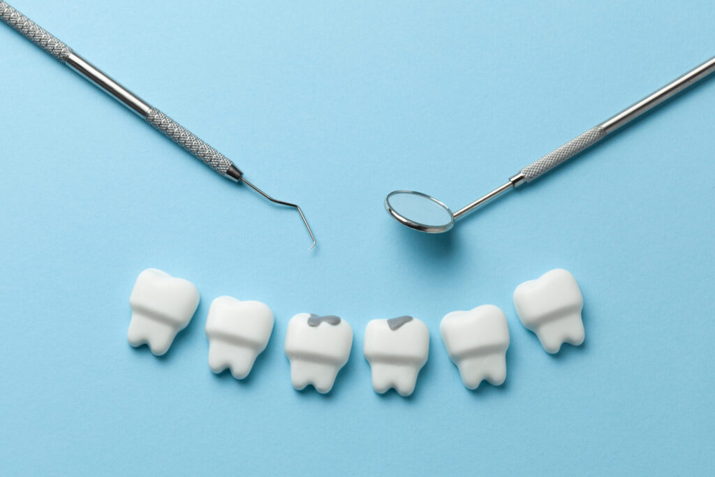 White tooth with caries on blue background and dentist tools mirror, hook