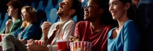 Happy friends enjoying in movie projection in theater. Focus is on African American woman eating popcorn.