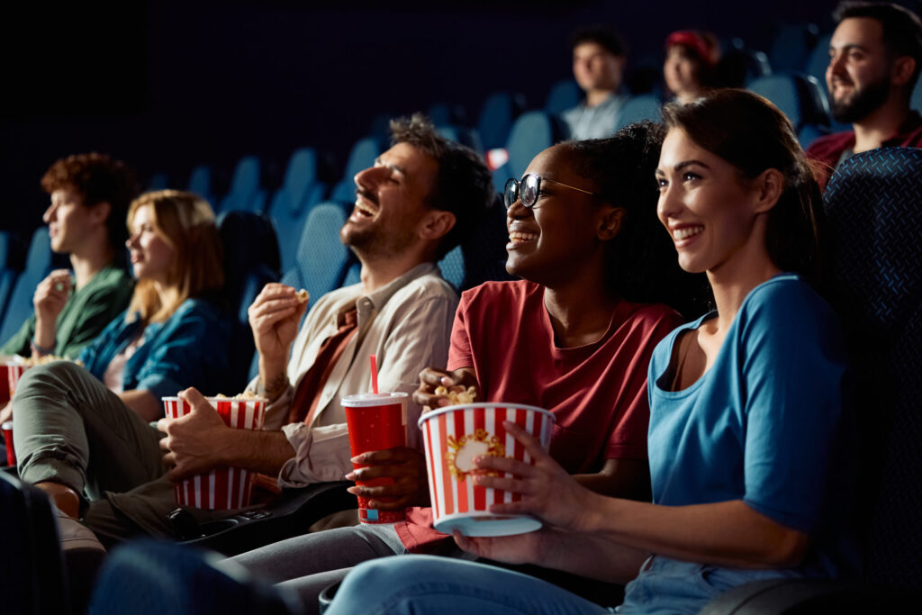 Happy friends enjoying in movie projection in theater. Focus is on African American woman eating popcorn.